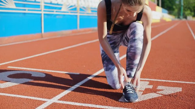 Sports young woman tying her shoelaces at outdoor stadium and starting to run
