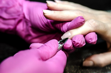 The process of cutting the cuticle using tweezers for manicure.