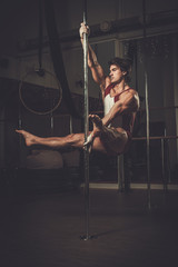 Handsome man performing pole dance moves on pole