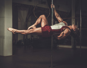 Handsome man performing pole dance moves on pole