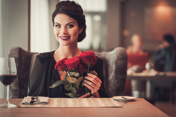 Elegant brunette lady with bouquet of red roses in restaurant