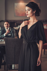 Elegant brunette lady in black evening dress in restaurant
