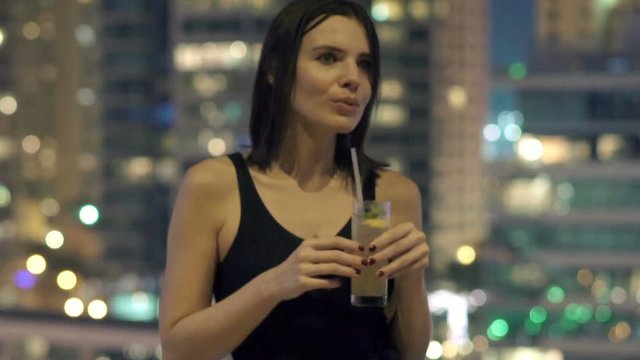 Young, beautiful woman drinking cocktail on terrace at night
