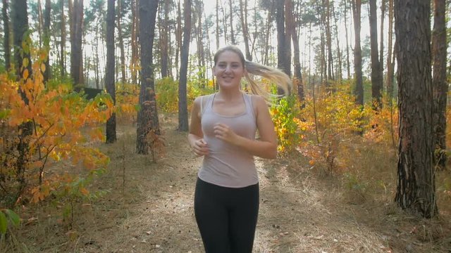 Slow motion closeup shot of happy smiling woman jogging at autumn forest