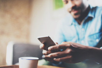 Young bearded African man using smartphone while sitting on sofa at home.Concept people working with mobile gadget.Selective focus hand.Blurred background.