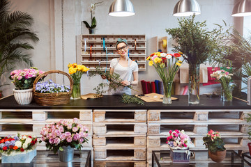 Happy beautiful young woman florist standing in flower shop