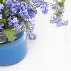 small blue flowers in a jar on a white wooden background