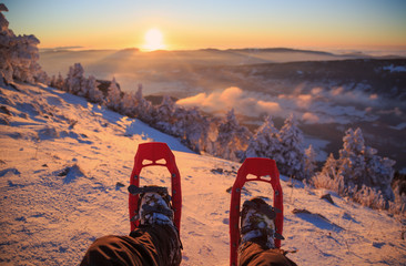 Winter sport activity. Male hiker looking over his snowshoes at the beautiful landscape in the French Vercors mountains during sunset.