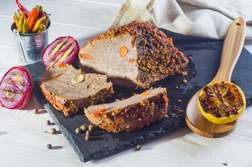 Roast pork with with mustard, onions and lemon on a white wooden table. Baked meat on a black slate board.