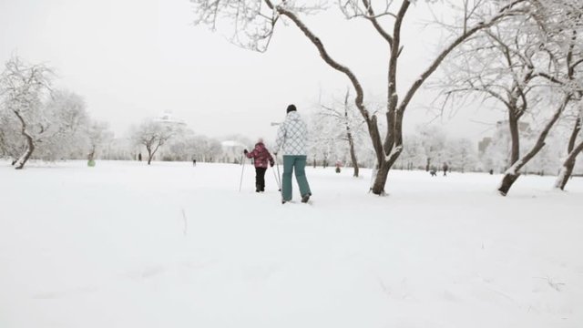 Russian people: mother and daughter run on skies. Skiing is in snowy urban park in winter
