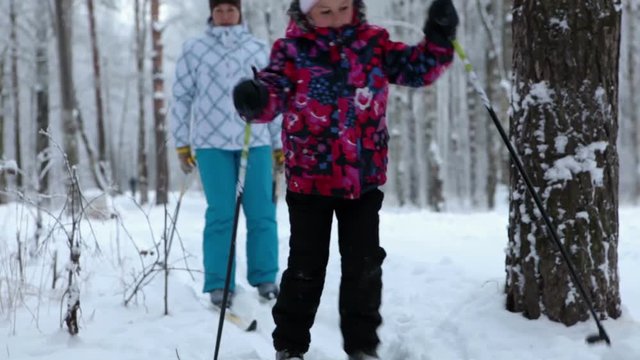 An adult mother and young daughter running on ski truck in snowy park. Winter season in Russia
