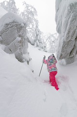 Маленькая девочка совершает зимой восхождение на гору.