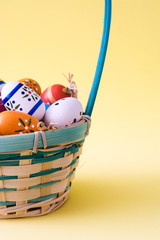 Colored easter eggs in a basket on yellow background
