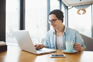 Handsome businessman in casual wear and eyeglasses is using a laptop in cafe