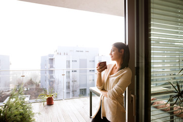 Woman relaxing on balcony holding cup of coffee or tea - obrazy, fototapety, plakaty