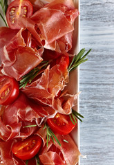  Prosciutto with  rosemary and tomato on a wooden table