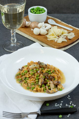Risotto with mushrooms and green peas. White plate, gray background, glass of wine.