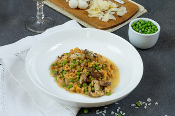 Risotto with mushrooms and green peas. White plate, gray background, glass of wine.