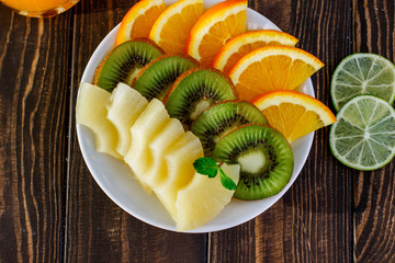 healthy eating plate of fresh fruit orange, kiwi, pineapple in a bowl on a wooden table