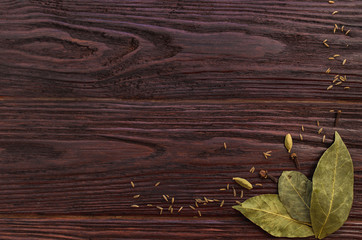 Bay leaves, cloves and caraway seeds on wooden dark textural bac