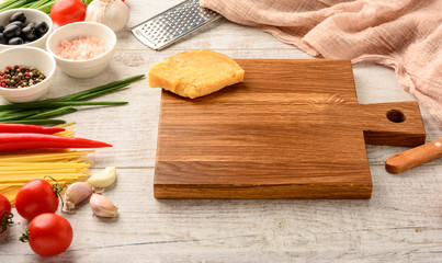 Ingredients for cooking healthy Italian food and cutting board on a white wooden table with space for an object in a home kitchen