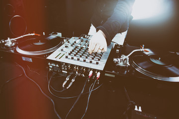 Club DJ playing mixing music on vinyl turntable at party wearing