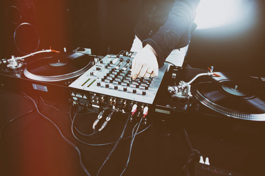 Club DJ playing mixing music on vinyl turntable at party wearing