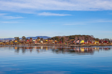 Fototapeta na wymiar Color wooden cabins on the island with sea at the foreground. Scandinavian style. Sunny winter day