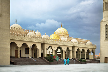 Fototapeta na wymiar Muslim mosque with two minarets cloudy weather, women going to i