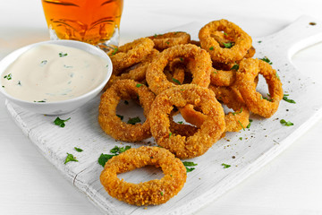Fried Breaded Onion Rings with sauce and Light Beer on white wooden board, background.