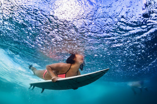 Active girl in bikini in action. Surfer woman with surf board dive underwater under breaking big wave. Healthy lifestyle. Water sport, extreme surfing in adventure camp on family summer beach vacation