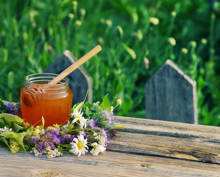 Honey in a glass jar with flowers melliferous herbs on a wooden surface. Honey with flowers.