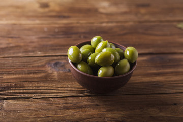 Green olives in a ceramic bowl on a wooden background. Background of olives. Background with green olives. Olives. Copyspace