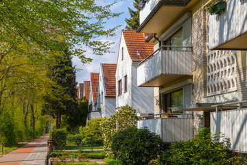 Modern german street with white stoned houses with tiled roofs. Sunny day and green alley.