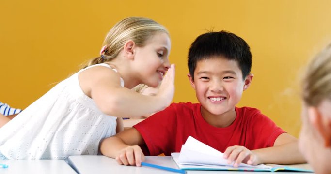 Schoolgirl whispering into his friend s ear in classroom at school 4k