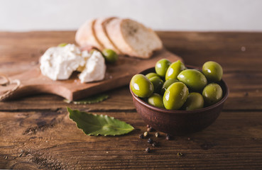 Green olives, sliced ciabatta, feta cheese on a wooden board. Spiced. Cheese Feta. Ciabatta. Olives on a light background