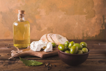 Green olives, sliced ciabatta, feta cheese on a wooden board. Olive oil in a glass bottle. Cheese Feta. Ciabatta. Olives on a orange abstract background