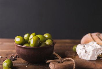 Green olives, sliced ciabatta, feta cheese on a wooden board. Cheese Feta. Ciabatta. Olives on a black  background