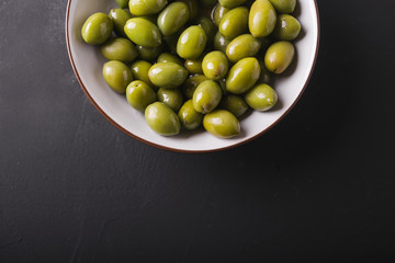 Green olives in a white bowl on a black background. Background of olives. Background with green olives. Olives. Bay leaf. Copyspace