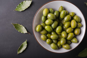 Green olives in a white bowl on a black background. Background of olives. Background with green olives. Olives. Bay leaf. Copyspace