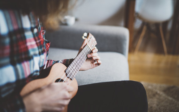 Young hipster girl sitting at cozy home interior at the morning and playing ukulele guitar, happy holidays, pretty woman learning to play ukulele guitar at vintage loft