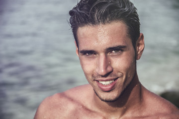 Attractive young man in the sea getting out of water with wet hair, looking in camera