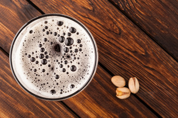 glass of dark cold frothy beer, nuts old wooden table