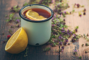 Tea in an iron mug, lemon, medicinal herbs on a wooden surface.