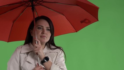  Chilled woman under red umbrella adjusting her coat against green screen. Maybe she is waiting for taxi or a bus at bus stop