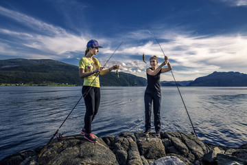 Girls standing on the rocks are excited about catched fish, Norw