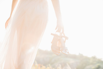 bride in wedding dress holding a shoes at sunset.