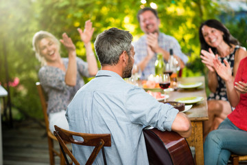 Summertime, man playing guitar for his friends on a terrace