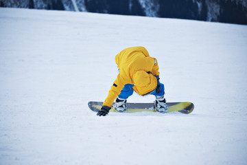 Snowboarder in yellow parka and blue pants stands up on slope after falling