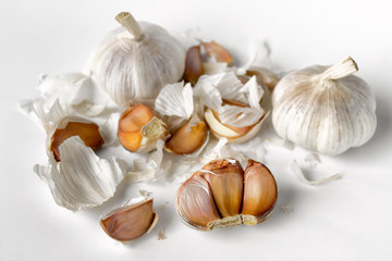 Organic garlic bulbs and separate cloves with messy white papery skins on white background.